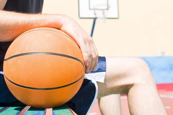 Jovem sentado em bancadas de campo de basquete — Fotografia de Stock