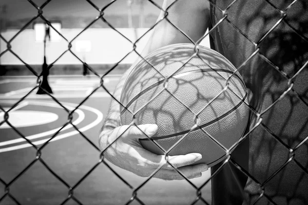 Молодой человек с баскетбольным мячом за забором — стоковое фото
