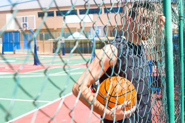 Jovem com uma bola de basquete atrás de uma cerca — Fotografia de Stock