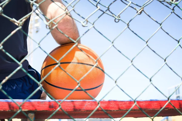 Jovem com uma bola de basquete atrás de uma cerca — Fotografia de Stock