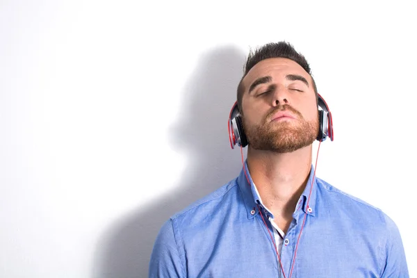 Man listening music with headphones. White wall with shadow — Stock Photo, Image