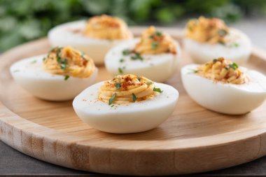 Homemade hard Boiled Deviled Eggs garnished with herbs on wooden table.