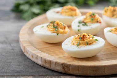 Homemade hard Boiled Deviled Eggs garnished with herbs on wooden table.