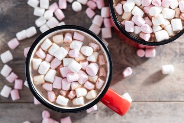 Sıcak çikolatalı içecek, marşmelovlu kırmızı bardak ve ahşap masa.