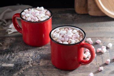 Sıcak çikolatalı içecek, marşmelovlu kırmızı bardak ve ahşap masa.