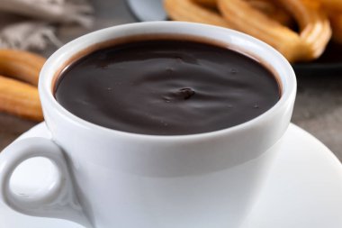 Beyaz bardakta sıcak, kalın çikolata ve ahşap masada churros.