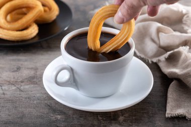 Beyaz bardakta sıcak, kalın çikolata ve ahşap masada churros.