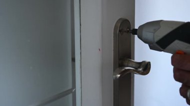 Kapı tokmağına vida takan pille çalışan kablosuz tornavidanın yakın çekimi.