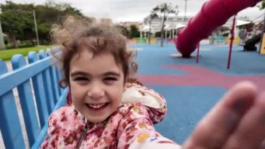 Mutlu küçük kız kameraya doğru koşuyor ve parkta gülüyor.