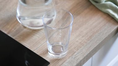 Temiz bir arkaplanda şeffaf bir bardağa temiz su dökülüyor. Tazelik, susuzluk ve günlük yaşamı gösteren basit bir eylem.