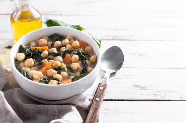 Ev yapımı nohut ve dilimlenmiş havuçlu ıspanak çorbası ahşap masada beyaz bir kasede servis edilir.