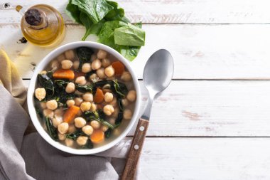 Ev yapımı nohut ve dilimlenmiş havuçlu ıspanak çorbası ahşap masada beyaz bir kasede servis edilir.