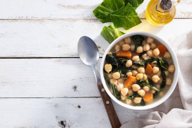 Ev yapımı nohut ve dilimlenmiş havuçlu ıspanak çorbası ahşap masada beyaz bir kasede servis edilir.