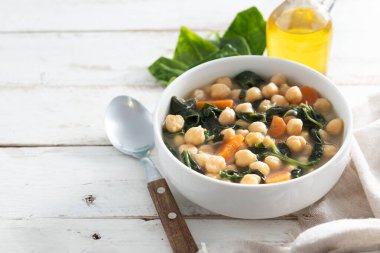 Ev yapımı nohut ve dilimlenmiş havuçlu ıspanak çorbası. Tahta masadaki beyaz kasede servis ediliyor. Boşluğu kopyala