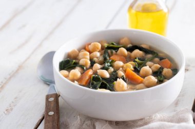 Ev yapımı nohut ve dilimlenmiş havuçlu ıspanak çorbası ahşap masada beyaz bir kasede servis edilir.