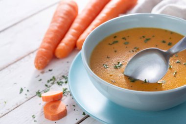 Ev yapımı kremalı havuç çorbası açık mavi bir kasede servis edilir, taze maydanozla süslenir ve kırsal beyaz ahşap bir masaya yerleştirilir..