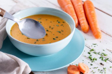 Ev yapımı kremalı havuç çorbası açık mavi bir kasede servis edilir, taze maydanozla süslenir ve kırsal beyaz ahşap bir masaya yerleştirilir..
