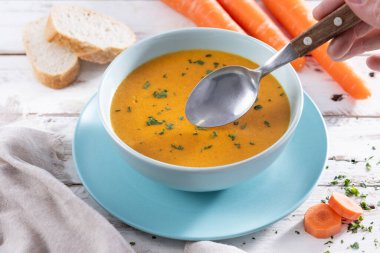 Ev yapımı kremalı havuç çorbası açık mavi bir kasede servis edilir, taze maydanozla süslenir ve kırsal beyaz ahşap bir masaya yerleştirilir..
