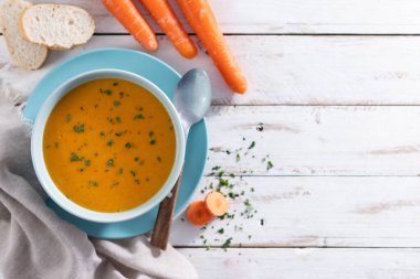 Açık mavi bir kasede servis edilen ev yapımı kremalı havuç çorbası. Taze maydanozla süslenmiş ve kırsal beyaz ahşap bir masaya konmuş. Üst Manzara. Boşluğu kopyala