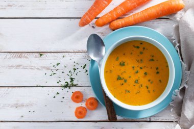 Açık mavi bir kasede servis edilen ev yapımı kremalı havuç çorbası. Taze maydanozla süslenmiş ve kırsal beyaz ahşap bir masaya konmuş. Üst Manzara. Boşluğu kopyala