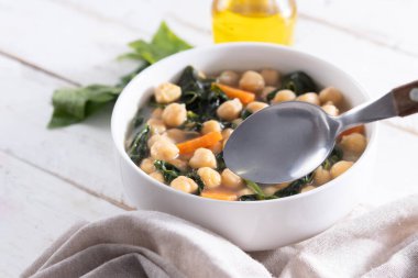 Ev yapımı nohut ve dilimlenmiş havuçlu ıspanak çorbası ahşap masada beyaz bir kasede servis edilir.