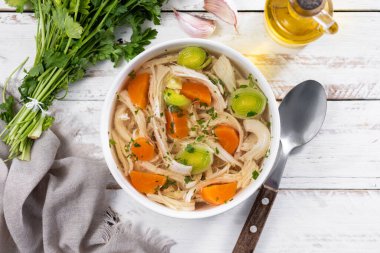 Beyaz kasede ev yapımı tavuk çorbası havuç ve ahşap masada kereviz.