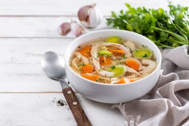 Beyaz kasede ev yapımı tavuk çorbası havuç ve ahşap masada kereviz.