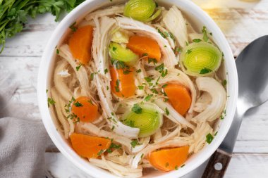 Beyaz kasede ev yapımı tavuk çorbası havuç ve ahşap masada kereviz.