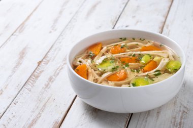 Beyaz kasede ev yapımı tavuk çorbası, beyaz ahşap masada havuç ve kereviz. Boşluğu kopyala