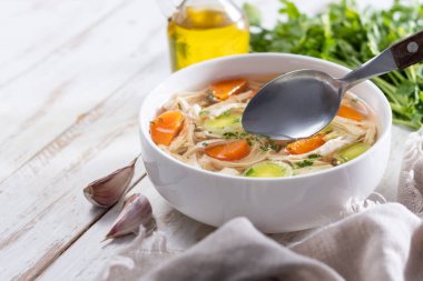 Beyaz kasede ev yapımı tavuk çorbası, beyaz ahşap masada havuç ve kereviz. Boşluğu kopyala