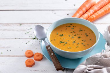 Beyaz ahşap masada mavi kasede kremalı havuç çorbası.