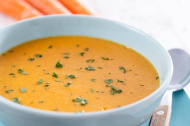 Beyaz ahşap masada mavi kasede kremalı havuç çorbası.