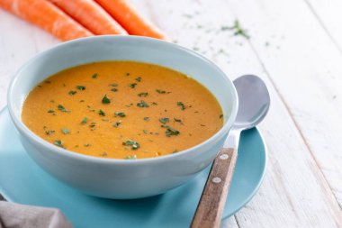 Beyaz ahşap masada mavi kasede kremalı havuç çorbası.
