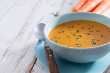 Beyaz ahşap masada mavi kasede kremalı havuç çorbası.
