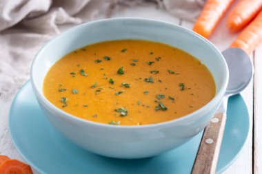 Beyaz ahşap masada mavi kasede kremalı havuç çorbası.