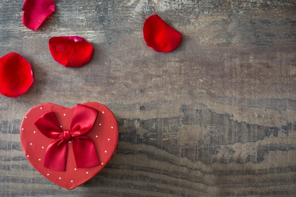 Geschenkdoos met hart vorm en bloemblaadjes op hout — Stockfoto