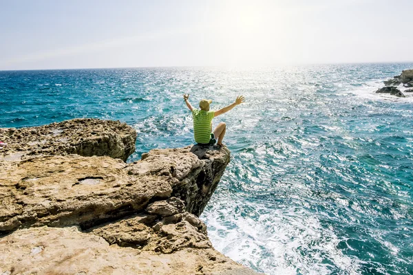 Un hombre se sienta en una cornisa de roca sobre el mar en el cabo Greco. Cypr — Foto de Stock