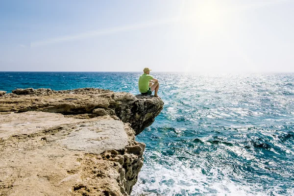 Een man zit op een richel van rots boven de zee bij Kaap Greco . — Stockfoto