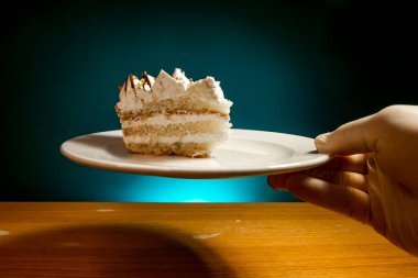 Beyaz tabakta bir parça kek mavi arka planda tıbbi eldivenli bir garson tarafından servis edilir.