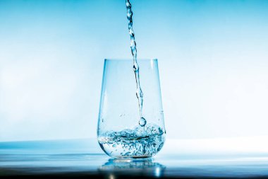 Bir tatlı su akıntısı mavi arka plandaki bir bardağa dökülür.