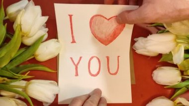 Adamın biri, seni sevdiğimi yazan bir kağıt parçasına turuncu arka plan manzaralı bir zarfın içinde mesaj bırakıyor. Uluslararası Kadınlar Günü. 4K görüntü.