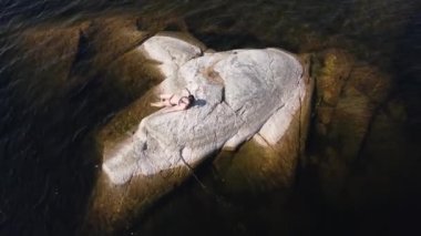 Rusya, Karelia 'da bir gölün ortasındaki taş bir adada güneşlenen bir kız..
