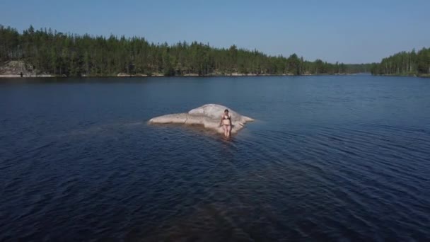 Uma menina toma banho de sol em uma ilha de pedra no meio de um lago na Carélia, Rússia. — Vídeo de Stock