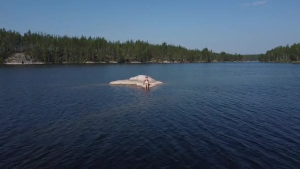 Uma menina toma banho de sol em uma ilha de pedra no meio de um lago na Carélia, Rússia. — Vídeo de Stock