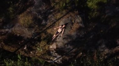 A girl sunbathes on a stone island in the middle of a forest in Karelia, Russia.