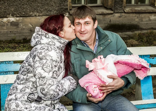 A couple of young parents with babies kissing on the bench — Stock Photo, Image