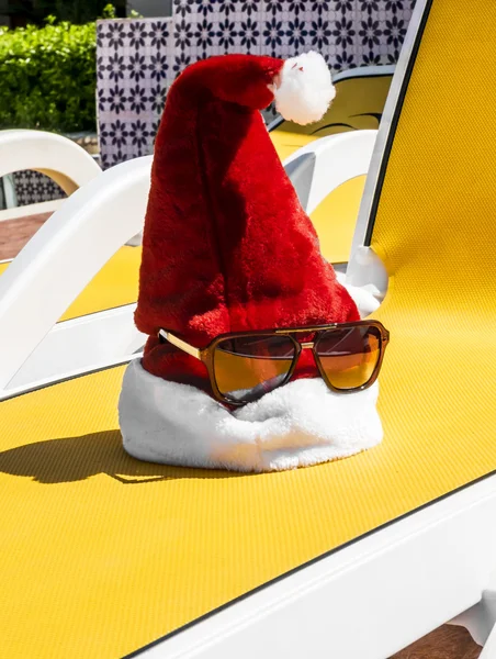 Chapeau de Père Noël avec des lunettes de soleil sur une chaise longue près de la piscine sur un tropique — Photo