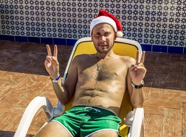 Un uomo con un cappello di Babbo Natale su un lettino a bordo piscina su una tropica — Foto Stock