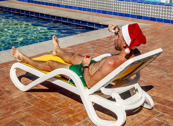 A man in a Santa's hat blows soap bubbles on the tropical resort — Stock Photo, Image