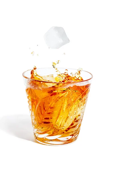 Ice cube falls with splashes into the glass with alcohol — Stock Photo, Image